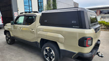 A black hardtop truck canopy installed on the bed of a beige Kia Tasman pickup truck, shown from the rear against a white studio background.