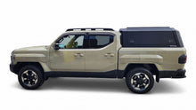 A black hardtop truck canopy installed on the bed of a beige Kia Tasman pickup truck, shown from the rear against a white studio background.