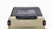 A black hardtop truck canopy installed on the bed of a beige Kia Tasman pickup truck, shown from the rear against a white studio background.