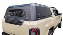 A black hardtop truck canopy installed on the bed of a beige Kia Tasman pickup truck, shown from the rear against a white studio background.