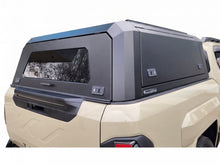 A black hardtop truck canopy installed on the bed of a beige Kia Tasman pickup truck, shown from the rear against a white studio background.