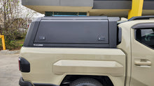 A black hardtop truck canopy installed on the bed of a beige Kia Tasman pickup truck, shown from the rear against a white studio background.