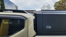 A black hardtop truck canopy installed on the bed of a beige Kia Tasman pickup truck, shown from the rear against a white studio background.
