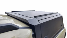 A black hardtop truck canopy installed on the bed of a beige Kia Tasman pickup truck, shown from the rear against a white studio background.